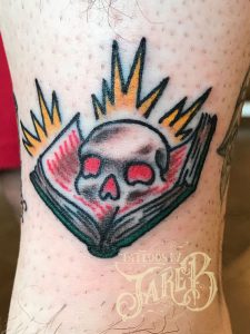 traditional skull & spell book tattoo by Jake B
